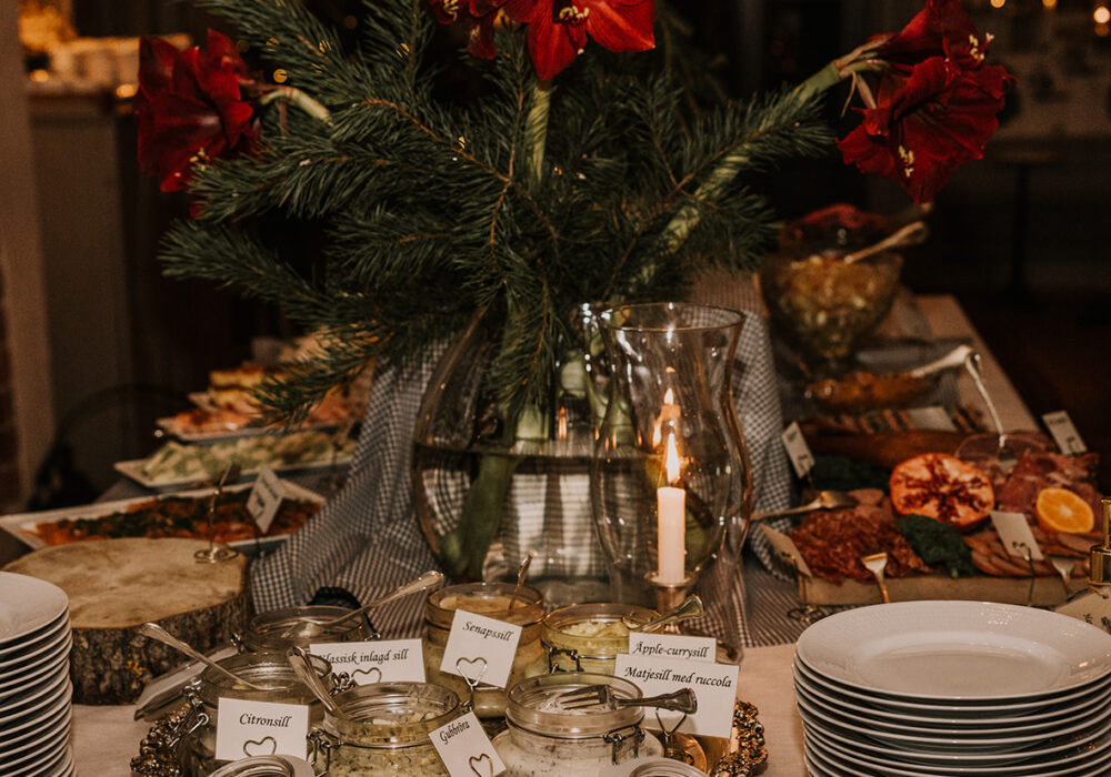 Ett stämningsfullt julbord med flera sorters sill i glasburkar, vackert dekorerat med röda amaryllis och granris.