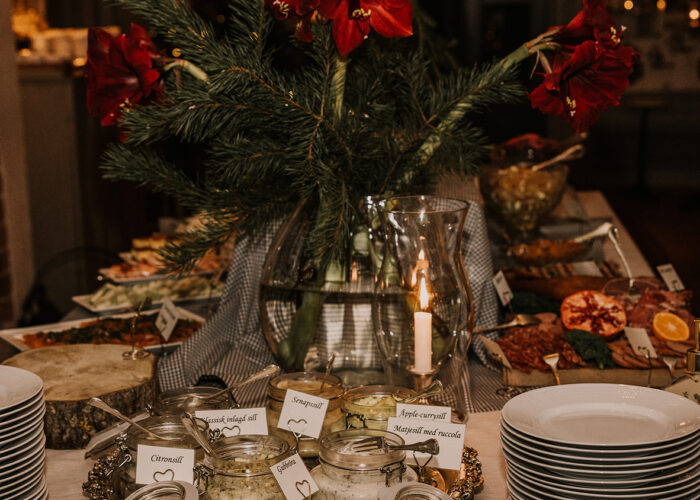 Ett stämningsfullt julbord med flera sorters sill i glasburkar, vackert dekorerat med röda amaryllis och granris.